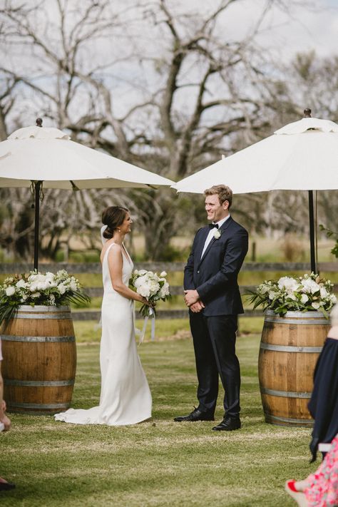 Wedding flowers by Scentiment Flowers, styling by Hire in Style, photo by Sarah Tonkin Photography, at Alverstoke Barn, south west Western Australia. Bride. Groom. Bridal bouquet. Boutonniere. Wedding ceremony. Ceremony flowers. Wine barrel flowers. Umbrella flowers. Green and white. Country wedding. Garden wedding. Farm wedding. Barn wedding. Summer wedding. Australian wedding. Historical property. Wine Barrel Alter Wedding, Wedding Ceremony Wine Barrels, Farm Wedding Australian, Wine Barrel Wedding Ceremony, Wine Barrel Wedding Flowers, Wine Barrel Flowers, White Country Wedding, Wine Farm Wedding, Flowers Umbrella