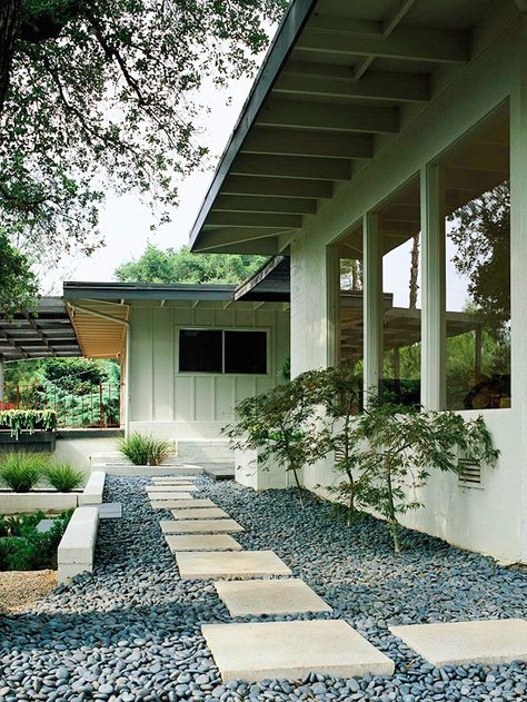 Side yard fix!   -- A short retaining wall bridges the divide between path and yard.  -- Gray river rock provides interest as filler between the pavers.  -- Irregularly placed flagstone pavers offer a path from front door around the side of the house.  -- A trio of Japanese maple trees provides visual texture; once full-grown, they'll create a delightful canopy over the path.  -- Chosen for their deep shade of green and unfussy structure, ornamental grasses play off the contemporary design. Grassless Yard, Texas Landscaping, Landscaping Around Trees, Front Yards Curb Appeal, Front Yard Decor, Walkway Landscaping, Halloween Decorations Outdoor, Landscape Inspiration, Front Yard Design