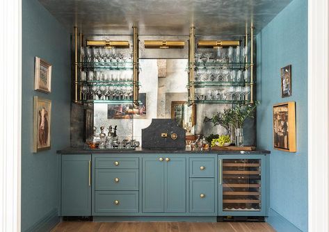 Wet bar features blue cabinets with glass and brass pipe plumbing shelves over antiqued mirrored backsplash panels, a honed black marble sink with a brass faucet mounted on a honed black marble backsplash and a mini wine fridge. White Leather Bar Stools, Mirror Decor Ideas, Dining Room Accents, Mirror Backsplash, Home Bar Designs, Beaver Creek, Blue Cabinets, Transitional House, Bespoke Interiors