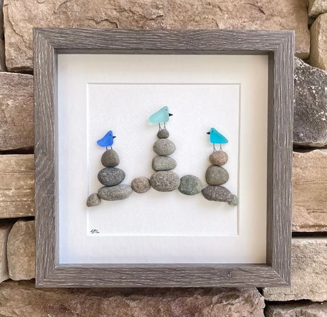 "Handmade sea glass and pebble art featuring 3 birds in shades of blue and turquoise sitting on rock cairns. Perfect gift for anyone that loves the beach / seaglass / hiking / coastal decor.  This artwork measures 8 x 8\" unframed and includes a high quality gray display case frame.  While you can find all of my ready-to-ship pieces of art currently on Etsy, I would be more than delighted to discuss custom projects to meet your needs. Feel free to reach out with questions at any time, I try to r Beach Rock Crafts, Rock And Sea Glass Art, Beach Glass Birds, Christmas Sea Glass Crafts, Sea Glass Crafts Ideas, Beach Glass Art Diy, Seaglass Art Ideas, Beach Rocks Crafts, Beach Art Diy