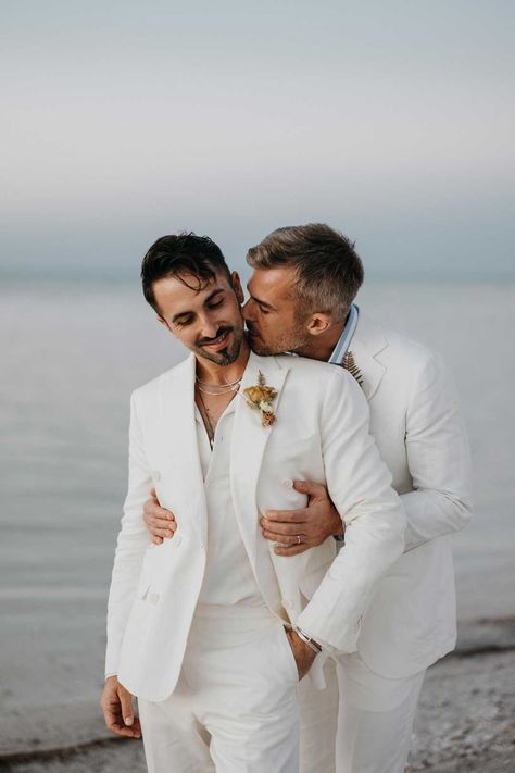 Groom in mens white wedding suit with dusky orange garden rose and dried flower boutonniere, white shirt and silver jewellery standing on the beach with Groom wearing white blazer, light blue and white striped shirt and dusky orange garden rose and dried flower boutonniere | LuxArt Wedding Studio Mens White Wedding Suit, Gay Wedding Outfits, Suit For Beach Wedding, Lgbtqia Wedding, White Wedding Suits For Men, Groom Blazer, Groom And Groomsmen Outfits, Weird Music, Weird Videos