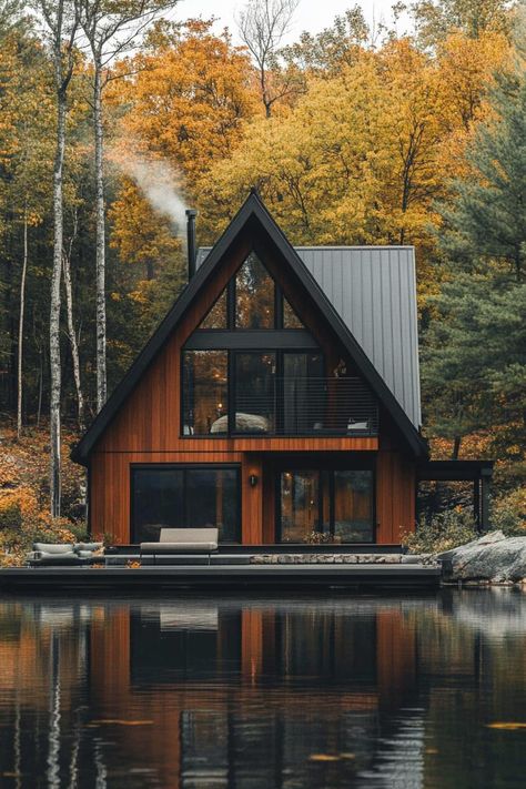 Modern a frame cabin with dark stained cedar siding large black frame modern windows and sliding doors grey metal roof in front of the house is a. Check out all of these stunning and chic dark A-frame houses that pack a ton of charm into a small forest retreat. Cabins With Metal Siding, Cabin With Black Trim, Small Village House Design, Black And Cedar House Exterior, Stained Cedar Siding, Grey Metal Roof, Modern Cabin Exterior, Modern Cabin In The Woods, Stained Cedar