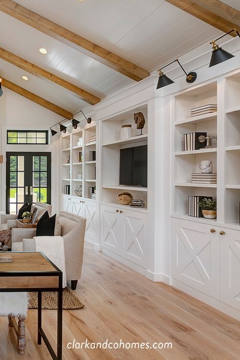 White oak flooring and ceiling beams, with white built-ins and accented by black light fixtures all contribute to the look of this Modern Farmhouse great room. #greatroom #modernfarmhouse #woodflooring #ceilingbeams #builtins #shiplapceiling Built Ins With Ceiling Beams, Built In Bookcase Lighting, Floor To Ceiling Entertainment Center, Built Ins With Sconces, Built In With Lights, Floor To Ceiling Built Ins, Modern Farmhouse Built Ins Living Rooms, Greatroom Builtins, Modern Farmhouse Built Ins