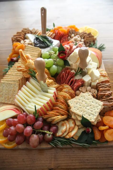 Looking for something to bring to a party? This Thanksgiving Charcuterie Board how-to has everything you need to create a professional cheese board in your home for just $60! With ingredients from Trader Joe's and a step-by-step assembly, you can have a professional cheese board presentation in time for your girls night appetizer spread or Thanksgiving dinner appetizers in no time. Start with cheese and meats, add fruit, layer in crackers, fill in gaps with nuts, and decorate with herbs and ... Cheese And Snack Board, Best Trader Joes Charcuterie, Snacks To Take To Work Party, Lunch Charcuterie Boards, Cheese And Cracker Charcuterie Board Ideas, Wine Tasting Cheese Board, Thanksgiving Charcuterie Board Trader Joes, Trader Joes Thanksgiving Charcuterie Board, Cheese Board Trader Joes