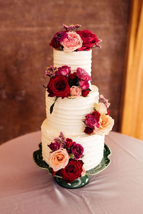 White three tiered wedding cake with ridged icing and pink and red floral cake decor. Frosted Wedding Cake, Layered Tulle Wedding Dress, Black Tie Wedding Reception, Wedding Cake Icing, Cake With Icing, Three Tier Wedding Cake, Elmore Court, Magenta Wedding, Wedding Bridesmaids Dresses Blue