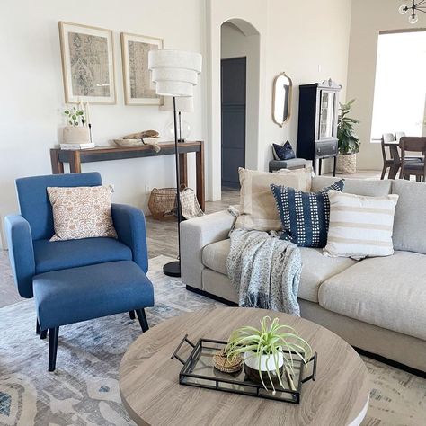 Black floor lamp with gray shade stands next to a gray couch accompanied by blue chairs for living room. A round stained wood coffee is placed in front of the couch on a white, gray and blue rug. Gray And Blue Farmhouse Living Room, Gray Couch With Blue Accent Chairs, Grey Couch Blue Pillows Living Room, Grey Suede Couch Living Room Ideas, Gray Couch Blue Accents, Gray Couch Pop Of Color, Dark Gray And Light Blue Living Room, Living Room Blue Accent Chairs, Grey Couch With Coffee Table