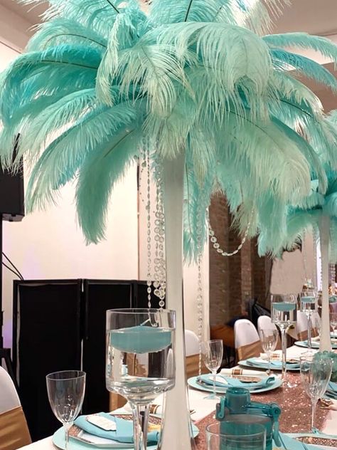 Impart a vigorous touch to your tablescape. Line a blush sequin runner in the middle of the table and arrange Eiffel Tower glass vases flaunting natural ostrich feathers and spruce it up with diamond strand to bring the vibrancy of natural hues and super dose of glimmer. Create an air of stately sophistication by further placing long stem candle holders along with turquoise napkins and take the elegance of your party chairs up by several notches by adorning them with velvet ruffle chair sashes. Party Decorations Table, Dream Setup, Feather Centerpieces, Home Decor Photography, Party Chairs, Event Decor Ideas, Event Look, Chair Sashes, Dinner Decoration