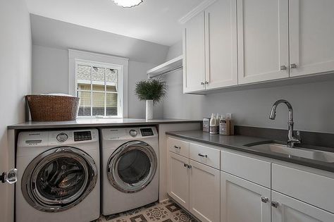 An enclosed white front loading washer and dryer sit beneath a gray quartz countertop mounted under a window framed by light gray wall paint. Front Loading Washer And Dryer, Gray Laundry Room, Washer Dryer Laundry Room, White Beveled Subway Tile, Laundry/mudroom Ideas, Cabinets To Ceiling, Grey Laundry Rooms, Laundry Room Update, Cabinets To Go