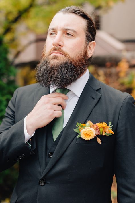 Solo portait of a groom with a beard and hair in a bun, wearing a black suit with a green tie and orange boutinnere pocket flowers. Pocket Flowers, Hair In A Bun, Black Suit Wedding, Groomsmen Ties, Black Tux, Orange Tie, Fall Weddings, Groomsmen Attire, Floral Photo