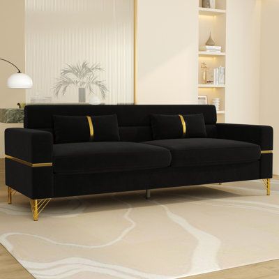 If you want a refined, style-forward piece for your living room, bar area, or sitting room, This modern velvet sofa is a great option. It has sleek, beautiful lines that give off a definite contemporary vibe. And it’s a gorgeous couch to look at, with its included throw pillows, jewel-toned color choices, and shining gold-hued legs. And don’t worry about assembly. It’s easy, since this couch only requires partial assembly on your part when it arrives. This made-to-order couch features foam blend Black White And Gold Family Room, Black Gold And White Living Room, Black Sofa Decor Ideas, Black Gold Sofa, Black And Gold Sofa, Black Sofas, Living Room Arm Chairs, Black Velvet Sofa, Tuxedo Sofa