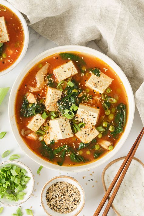 A bowl of tofu soup garnized with chopped green onions, sesame seeds, and chili flakes.