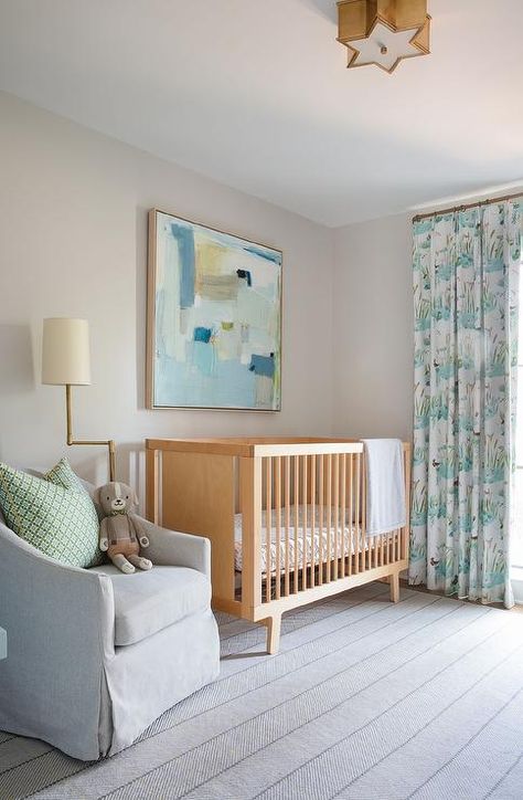 A yellow and blue abstract art piece hangs in a lovely nursery above a blond vintage crib placed between a window dressed in white and blue curtains and a pale gray slipcovered glider topped with a green trellis pillow and lit by a brass swing arm floor lamp. White And Blue Curtains, Art Above Crib, Transitional Nursery, Green Trellis, Vintage Crib, Dressed In White, Blue Curtains, Blue Abstract Art, Arm Floor Lamp