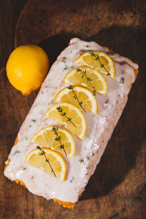 Lemon and Thyme Cake is topped with lemon and thyme glace icing, slices of lemon and sprigs of thyme. It is lying on a dark wood board with a whole lemon to its left. Lemon Thyme Cake, Lemon Thyme Recipes, Thyme Cake, Vegan Lemon Cake, Vegetarian Mains, Thyme Recipes, Dad Birthday Cakes, Savory Scones, Lemon Drizzle Cake