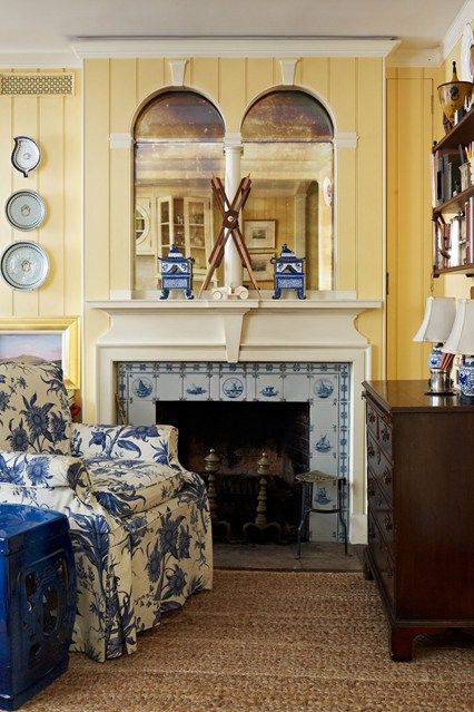 Yellow paneled room features a delft tile fireplace surround and a blue and white toile chair – photo: Lucas Allen – House & Garden Tile Bedroom, Sweden House, Urban Cottage, Fireplace Tile Surround, Delft Tiles, New York Homes, Fireplace Surround, White Cottage, French Cottage