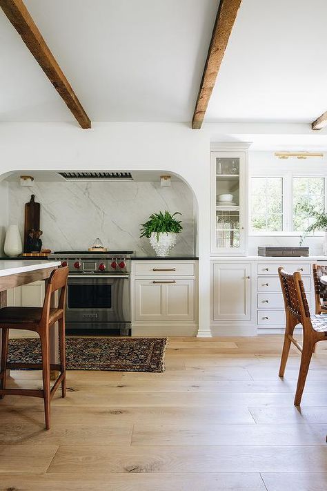 A curved stone cooking alcove is fitted with a Wolf range placed between light gray kitchen cabinets adorned with aged brass hardware and contrasted with a black countertop. Oven Alcove, Stove Alcove, Kitchen Trends 2021, Alcove Ideas, Jean Stoffer Design, Tudor Kitchen, Jean Stoffer, Top Kitchen Trends, Family Room Remodel