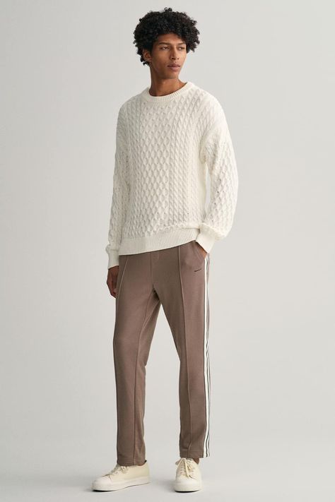 Men's brown trackpants, white cable knit sweater and off-white canvas sneakers outfit. This outfit was included in the article: How To Wear Brown Pants: 18 Outfit Examples & The Colours That Go Best, on MensFlair.com White Cable Knit Sweater Outfit Men, Canvas Sneakers Outfit, Black Pants Outfit Men, Blue Shirt Black Pants, Cable Knit Sweater Outfit, Brown Pants Outfit, Outfit Rock, Sweater Outfits Men, Black Pants Outfit