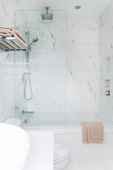 A polished nickel towel rack is mounted to a marble clad wall above a toilet positioned beside a drop in wainscoted tub fitted with with a glass partition and marble wall tiles surrounding tiled niches fixed facing a polished nickel exposed plumbing shower kit paired with a rain shower head. Kids Bathrooms, Bathtub Shower Combo, Small Shower Remodel, Wainscoting Bathroom, Refinish Bathtub, Bathtub Tile, Brick Ranch, Tub Tile, Transitional Bathroom