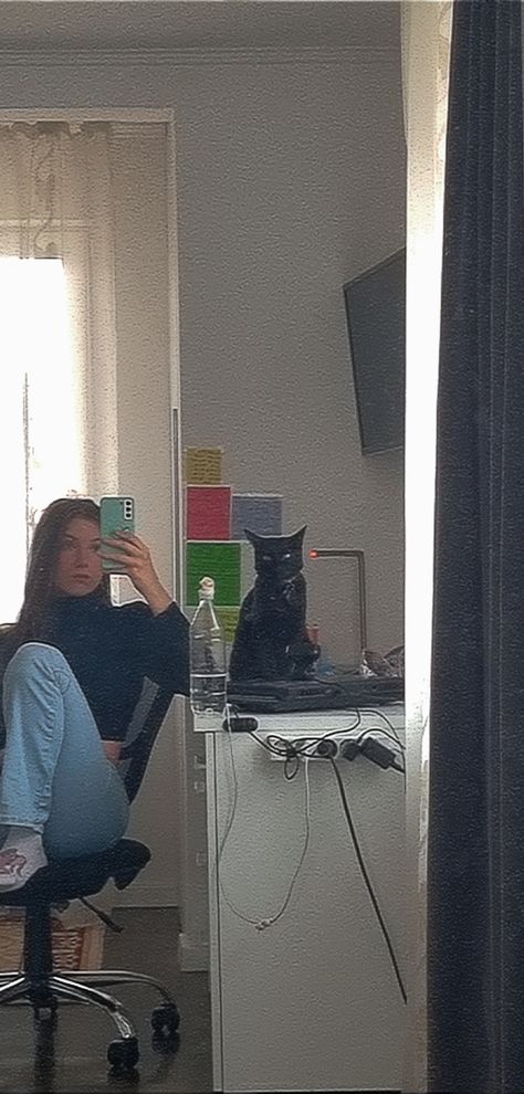 A mirror selfie , the black cat sits on the desk and the owner (a girl wearing a black turtleneck) matches the cat height by sitting on the desk's chair with a leg on it.Everything else in the background  is light colored contrasted by a grainy indie filter (highly saturated colors ). Height Difference, Chair Pose, Mirror Selfie Poses, A Mirror, On The Ground, Selfie Poses, A Chair, Your Pet, A Cat