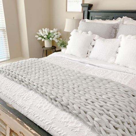 The white and gray linens on this rustic bedframe with chipped paint are so inviting. A textured white comforter with pom pillows lays beneath a knit rug made with oversized yarn. The texture that is pulled out of this throw blanket makes a statement against beige walls, and is the perfect pop of gray in a room based on various neutrals. Bed With Lots Of Pillows, Rustic Bedframe, Mismatched Bedroom Furniture, Mismatched Bedroom, White Bedroom Cozy, Throw Rugs Bedroom, Gray Bedroom Ideas, White Nightstands, Grey And White Bedding