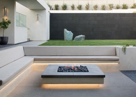 A clean, modern fire pit is flanked by a built-in bench topped with custom cushions that blend into the calm, neutral color palette. A pair of sculptural boulders become art when placed before a dark garden wall, which edges an elevated pool. Kursi Outdoor, Sunken Fire Pits, Modern Fire Pit, Backyard Seating, Garden Fire Pit, Modern Landscape Design, Modern Backyard, Backyard Fire, Modern Patio