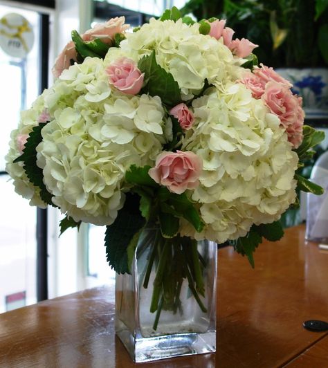 Low centerpiece of white hydrangeas, pink roses and pink spray roses in a vase with exposed stems. Hydrangea Centerpiece Diy, Diy Hydrangea, Hydrangea Centerpiece, Hydrangea Arrangements, Joel Osteen, Flower Arrangements Diy, Fresh Flowers Arrangements, Beautiful Flower Arrangements, Spray Roses