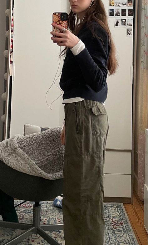 Mirror selfie pic of girl with long brunette brown hair standing side ways profile to mirror wearing navy blue sweatshirt, white long sleeve T-shirt underneath peaking out under and green khaki cargo baggy 90s pants trousers. Fun, funky, cool outfit inspo, winter outfit ideas, layering, clothes, pretty, cute, 90s outfit idea. Holding phone with apple wired white headphone attached. 70s funky floral orange brown yellow phone case. Pic inspo, picture inspiration, photo ideas, instagram idea Green Parachute Pants Outfit Winter, Khaki Parachute Pants Outfit, Green Pants Aesthetic, Khaki Green Pants Outfit, Parachute Pants Outfit Winter, Green Parachute Pants Outfit, Personal Rebranding, Green Carpenter Pants, Beige Puffer Jacket