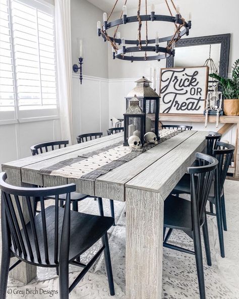 This gray farmhouse dining room with a white board and batten half wall features a gray wood dining table. The table is accompanied by black spindle chairs lit by a black two tier wagon wheel chandelier and black wall sconce. Board And Batten Dining Room, Modern Outdoor Dining Table, Charming Dining Room, Dining Room Accent Wall, Dining Room Accents, Room Accent Wall, Walnut Dining Chair, Woodworking Project Plans, Black Dining Chairs