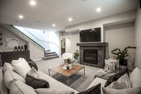 This modern living room features a grey stone fireplace and dark wood mantel, and uses grey shades throughout the room to create a warm and cozy atmosphere. Grey Basement, Grey Stone Fireplace, Gray Basement, Basement Living Room, Wood Mantel, Basement Living, Basement Living Rooms, Grey Shades, Floating Staircase