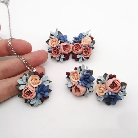 Celebrate the eternal bloom of spring with this exquisite polymer clay flower jewelry set. Each piece in this set - a pendant necklace, a pair of pousette earrings - is a meticulously handcrafted bouquet of delicate roses, peonies, succulents and fragile leaves in a pastel palette of soft peach, serene blue and earthy red. A necklace with a lush bouquet of flowers is suspended from a delicate silver-tone chain, lending a nature-inspired elegance to any outfit. The matching earrings are designed as studs, each featuring a small arrangement of flowers, harmoniously complementing the necklace. Created with attention to detail, these lightweight and durable polymer clay pieces are perfect for adding botanical charm to your everyday closet or for a special occasion, perfect for a wedding outfit Polymer Clay Wedding Jewelry, Clay Flower Jewelry, Blue Range, Clay Embroidery, Polymer Clay Flower Jewelry, Roses Peonies, Clay Pieces, Book Earrings, Dress Book