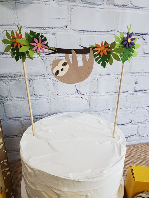 "Sweet and slow, a sloth themed party is perfect for baby showers or birthday parties.  Create the cutest little sloth party with this adorable sloth cake topper.  The topper features a little light brown sloth hanging from a limb with tropical foliage.  The sloth and foliage are made from 80-pound cardstock and strung on jute twine.  The sloth measure approximately 2 ¼\" x 3\", with the foliage the topper measures approximately 9 ½\" across and the bamboo sticks are approximately 9\" tall.  In the photos the topper is on an 8\" diameter cake.      Don't see the colors or quantity you want?  Convo me for availability of personalized options and to set up a custom order.     All products in my shop are made to order, meaning I make them especially for YOU!  Because of this I have a NO retur Sloth Bday Party Ideas, Sloth Birthday Cake, Sloth Birthday Party, Jungle Cake Topper, Sloth Cake, Sloth Cakes, Sloth Party, Animal Themed Birthday Party, Sloth Hanging