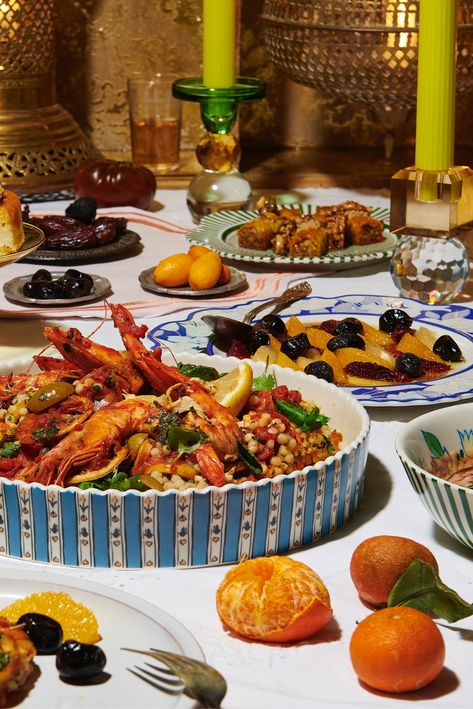 A spread of Moroccan dishes on a table. In the foreground, peeled clementines and a prawn tagine in a blue and white serving dish. In the background, a citrus and olive salad, goat cheese cigars, a dish of kumquats, long candlesticks, and Moroccan lanterns. Moroccan Dinner Party, Dinner Hosting, Dinner Host, Eastern Cuisine, Dinner With Friends, Ramadan Decorations, Social Interaction, Couscous, Party Inspiration