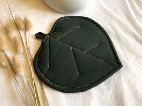 "A sweet potholder shaped like a leaf, and quilted to look like leaf veins.  The outer fabric is a dark emerald green cotton and the inner layers are Insul-bright, which is heat resistant up to 400 degrees Fahrenheit, and a layer of cotton batting.   🌿Potholder is NOT microwaveable🌿 ✨Find the matching coaster set in my shop!  This would make a beautiful addition to any \"outside-in\" kitchen, and is wrapped, ready to gift, in all eco friendly packaging!  🌻 The dimensions are approximately 8x8 Jungle Kitchen, Botanical Kitchen, Leaf Veins, Kitchen Trivets, Dark Emerald Green, Washer Machine, Eco Friendly Packaging, Pot Holder, Trivets