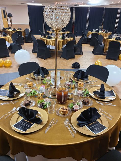 Add a glamorous black and gold touch to your décor by dressing up the tables using gold overlays and placing square mirrors as bases for eye-catching tall goblet candle holders positioned in the middle along with gold votive candle holders on the tables. For the finest place setting, arrange gold chargers, black napkins, & silver cutlery. Further, beautify the ambiance with gold and white balloons and black curtains. Also, outfit the chairs using black covers for a classy decor. Gold Votive Candle Holders, Black Napkins, Gold Chargers, Classy Decor, Black Curtains, Square Mirror, White Balloons, Votive Candle Holders, Touch Of Gold