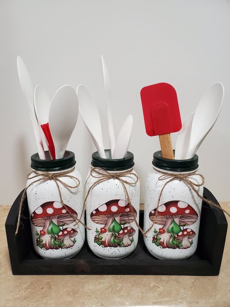 This set of mason jar utensil holders comes with the three quart size brand new anchor hocking jars, and the wooden box. Each jar is hand painted using white cotton chalk paint. The pictures of the mushrooms have been printed out onto tissue paper, and applied by using the decoupage technique. They are speckled with a dark green acrylic paint, and the rims are painted dark green to match. Then several coats of a satin varnish is applied. A jute twine bow is tied around the neck of each jar, and Mushroom Kitchen Theme, Mushroom Kitchen Decor, Mushroom Things, Mushroom Stuff, Mason Jar Utensil Holder, Mushroom Kitchen, Mason Jar Kitchen Decor, Cow Kitchen Decor, Kitchen Revamp