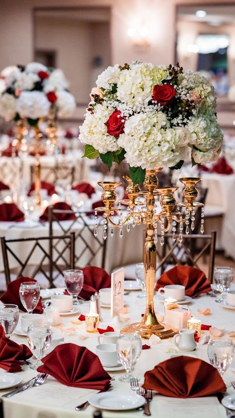 Romantic red and ivory floral wedding centerpieces on bronze metallic stand with hanging acrylic beads. Classic white tablecloth with luxury red napkins decorated with red rose petals and glassware. Wine Gold And White Wedding Decor, Champagne And Red Wedding Decorations, Ivory Red And Gold Wedding, Red And White Aesthetic Wedding, White Gold And Red Wedding Decor, White And Bronze Wedding Decor, Red White And Gold Wedding Reception, Red And White Roses Wedding Decor, White Red Wedding Decoration