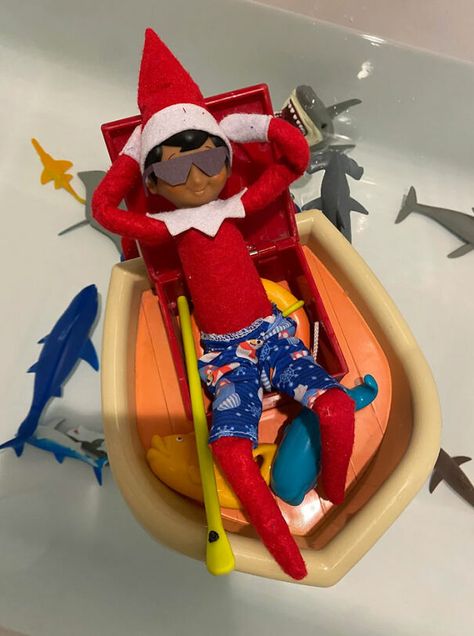 "Elf On The Shelf idea featuring an elf relaxing in a toy boat wearing sunglasses and swim trunks, surrounded by toy sharks in a bathtub." Elf On The Shelf On A Cruise Ship, Beach Elf On The Shelf, Elf On The Shelf Cruise Ship, Elf On The Shelf On A Cruise, Elf On The Shelf Return, Funny Elf On The Shelf, Elf Ideas Easy, Elf On A Shelf, Christmas Golf