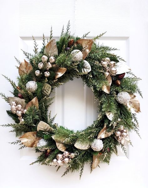 "This beautiful champagne and gold magnolia winter wreath is the perfect way to welcome guests into your home during the holiday season. It may also be used as a lovely accent for a winter wedding. This wreath includes champagne and gold magnolia leaves, large champagne gold berry clusters, gold tipped cedar, icy gold glitter ornaments, and pinecone ornaments nested in a pine wreath base form. Due to shipping, this item measures approximately 20\" in diameter and may need some slight \"fluffing\ Christmas Wreaths Gold And Silver, Christmas Wreaths For Front Door With Ornaments, Silver And Gold Wreath, Silver And Gold Christmas Wreath, Gold Christmas Wreath For Front Door, Black And Gold Christmas Wreath, Christmas Decor White And Gold, White And Gold Wreath, Gold And Green Christmas