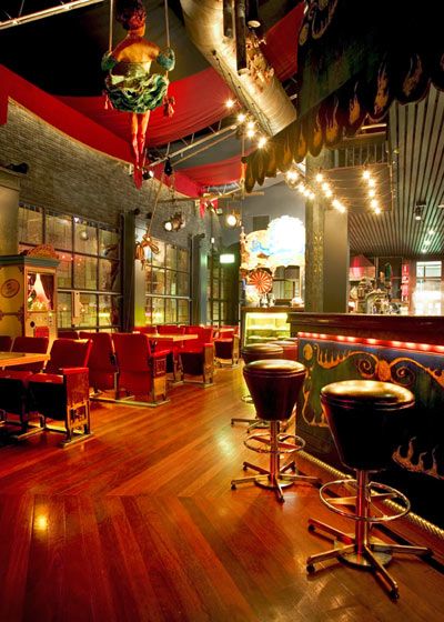 Vibrant, oppulent circus themed room adorned with bright stage lights and red embelishments with trapeze artist on a swing Circus Themed Restaurant, Circus Restaurant, Circus Interior, Circus House, Aerial Studio, Circus Room, Bar Events, Arcade Bar, Boho Bar