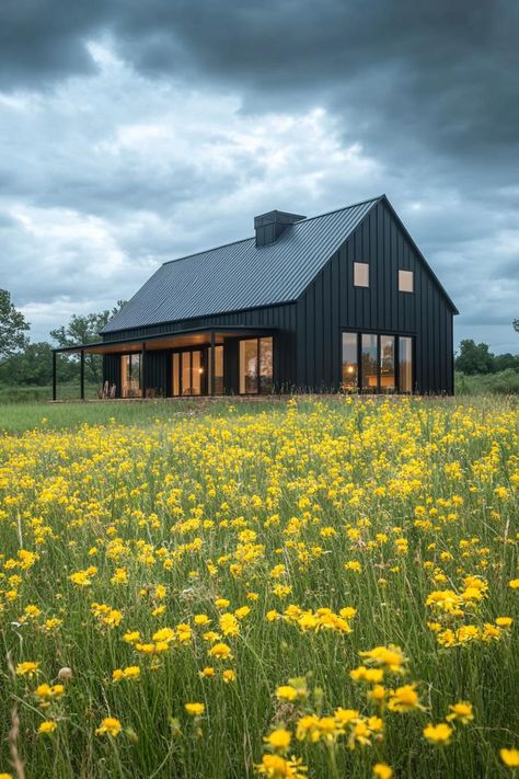 Modern barndominium charcoal black facade in stunning farmhouse meadow with yellow flowers. Check out the coolest dark barndominium houses that combine rustic charm with modern sophistication, enhancing a living space with bold hues and sleek designs. Barndominium With Screened In Porch, Contemporary Barndominium Ideas, Black And Cedar Barndominium, Dark Colored Barndominium, Barndominium Lake House, Barndominium 2 Story, Barndominium Landscaping, Steel Homes Metal Houses, Dark Barndominium