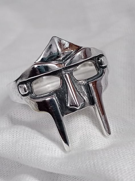 Unleash your inner villain with the Silver MF DOOM Ring, a true rap aficionado's dream come true. Paying homage to rap legend MF DOOM and his iconic villain mask, this silver gladiator ring is designed to make a statement. The antique finish and intricate detailing on the ring's face give it a timeless yet edgy appeal. Its lightweight design ensures comfort while adding an air of mystery and rebellion to your style. Perfect for gifting during the holiday season, this ring will make any hip-hop e Cool Rings For Men Unique, Rings For Men Aesthetic, Rapper Rings, Doom Ring, Gladiator Ring, Mf Doom Ring, Villain Mask, The Ring Face, Mf Doom