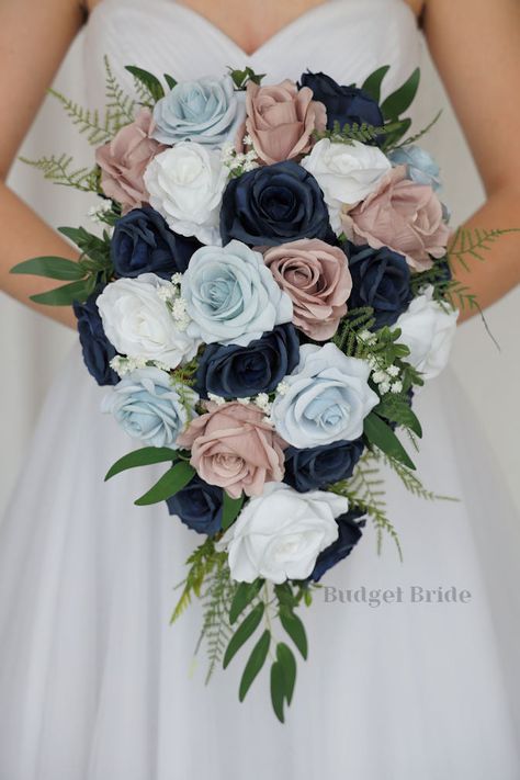 This lovely assortment of navy blue, mauve, dusty blue and white roses is bound to turn heads on your wedding day. This lovely cascading brides’ bouquet from the is an absolutely breathtaking arrangement for any bride to be, in any season. Bright greenery and babies breath complete the look and add a delicate realism to this beautiful bouquet. This bouquet is 10” wide, 18” long, and is crafted by our in-house florists without using a foam base to anchor the flowers to the bouquet. Instead, we wi Champagne Wedding Flowers, Small Bridesmaid Bouquets, Fake Wedding Flowers, Mauve Roses, Blue And White Roses, Sage Eucalyptus, Fresh Wedding Flowers, Fake Wedding, Budget Bride