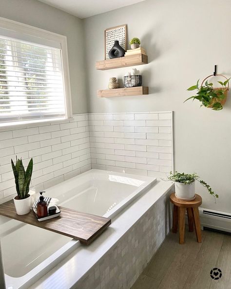 White framed window provides this neutral bathroom with natural light. White tile surrounds an alcove bathtub with wood accents arranged within this space. Bathroom floating shelves are affixed to the wall. White Bathrooms With Wood Accents, Bathtub Wall Shelf, Floating Shelves Above Tub, Tub Wall Ideas, Shelves Over Tub, Bathtub Wall Decor, Bathroom 2024, Built In Bathtub, Built In Bath