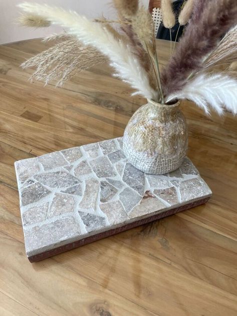 I had some leftover tile pieces and a piece of timber so decided to make a mosaic tiled table centrepiece! This would make a really good gift too. Firstly find a piece of timber for the base of the centrepiece. I had this travertine tile leftover from our pool landscaping. It’s a beautiful stone tile, I just needed to break it up into smaller pieces. To do this I dropped it onto the ground, then used a hammer to break it into smaller pieces. I then tested the design prior to g… Mosaic Gift Ideas, Tile Diy Projects, Leftover Tile Projects, Diy Mosaic Tiles, Tiled Table, Tile Mosaic Art, Leftover Tile, Trivets Diy, Mosaic Tile Table