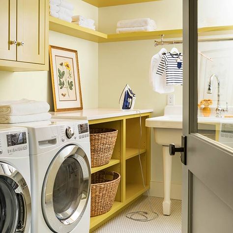 A cream laundry room with built-in shelves and cabinets in a midtone yellow color. Yellow Mudroom Cabinets, Mustard Yellow Laundry Room, Pale Yellow Laundry Room, Yellow Cabinets Laundry Room, Light Yellow Laundry Room, Yellow Laundry Room Ideas, Small Laundry Room Paint Colors, Yellow Laundry Room, Yellow Wallpaper Laundry Room