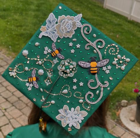 Aesthetic green emerald honey bee themed simple elegant graduation cap decoration with flowers and rhinestones, pearls and bee decals that is sparkly Green Graduation Aesthetic, Graduation Cap Ideas Simple, Elegant Grad Cap Ideas, Graduation Cap Simple Design, Bee Graduation Cap, Grad Cap Inspo High School, Flower Graduation Cap Designs, Grad Caps Aesthetic, Pretty Grad Caps