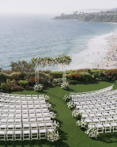 Say "I do" with the ocean as your backdrop in this breathtaking beachside wedding ceremony setup. With lush greenery, elegant white chairs, and a beautifully adorned floral arch, this setting offers the perfect combination of natural beauty and refined elegance. Ideal for couples looking to tie the knot in a serene and picturesque location by the White Chairs Wedding, Katb Ketab, Summer Wedding Venues, Wedding Ceremony Setup, Natural Wedding Decor, Ocean Background, Wedding Altar, Altar Ideas, Beachside Wedding