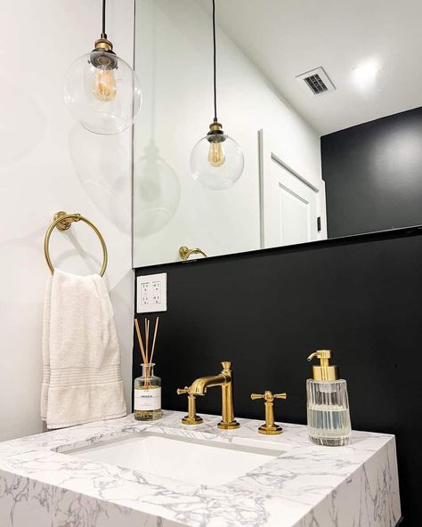 This powder room appears luxurious and modern with gold accets, a large mirror, and a marbled sink countertop. Contrasting against the black backdrop, the customized golden faucet pops out even more. Black And Gold Powder Room, Room With Gold Accents, Luxurious Powder Room, Room Wall Colors, Powder Room Decor, Black Backdrop, Sink Countertop, Gold Powder, Black Backdrops