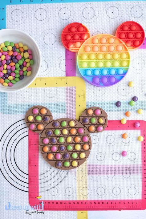 Image shows a colourful background of rainbow silicone baking sheets and a bowl of skittles sweets, a pop-it toy in the shape of Disney's Mickey Mouse and a chocolate bar made out of skittles and chocolate. Image by Keep Up With The Jones `Family Pop It Chocolate Bar, Pop It Chocolate, Food Network Chefs, 10 Birthday Cake, Chocolate Pops, Kids Cooking Recipes, Jones Family, Mickey Party, Candied Nuts