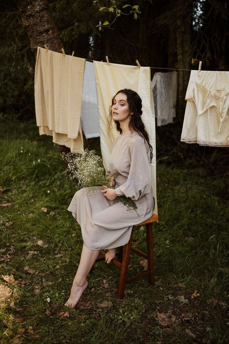 Model is seated on a stool with one foot tucked up and one forward on ground. Model holds a bouquet of baby's breath, and a clothesline with neutral sheets hangs behind her. Laundry Line Photoshoot, August Photoshoot Ideas, Clothes Line Photoshoot, Clothing Line Photoshoot Ideas, Summer Editorial Photoshoot, Clothesline Photoshoot, Laundry Photoshoot, Backyard Photoshoot, Dog Photoshoot Pet Photography