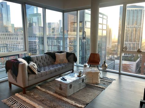 Modern living room with floor to ceiling windows, hardwood floors, concrete ceilings, grey suede couch, shag ottoman, metal trunk coffee table, red leather lounge chair, white fur throw pillows, and city views | Domu Chicago Apartments Grey Suede Couch, Floor To Ceiling Windows Apartment, White Fur Throw, Boujee Bedroom Ideas, Living Room Wallpaper Ideas, Apartamento New York, Room Wallpaper Ideas, Suede Couch, City Apartment Decor